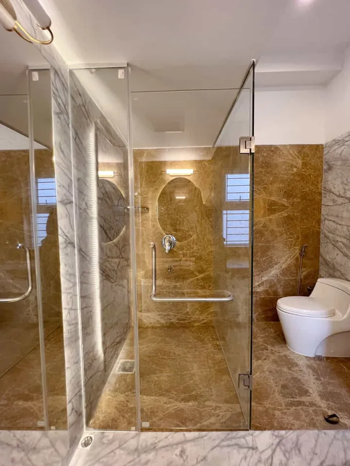 Clear glass shower enclosure in a warm stone-lined bathroom